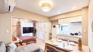 A modern, well-lit room with a sofa, a dining table set for four, a TV, and a kitchen area with a microwave and stove. - Triphome Asakusa Alpha 2 Bedrooms (Taito City)