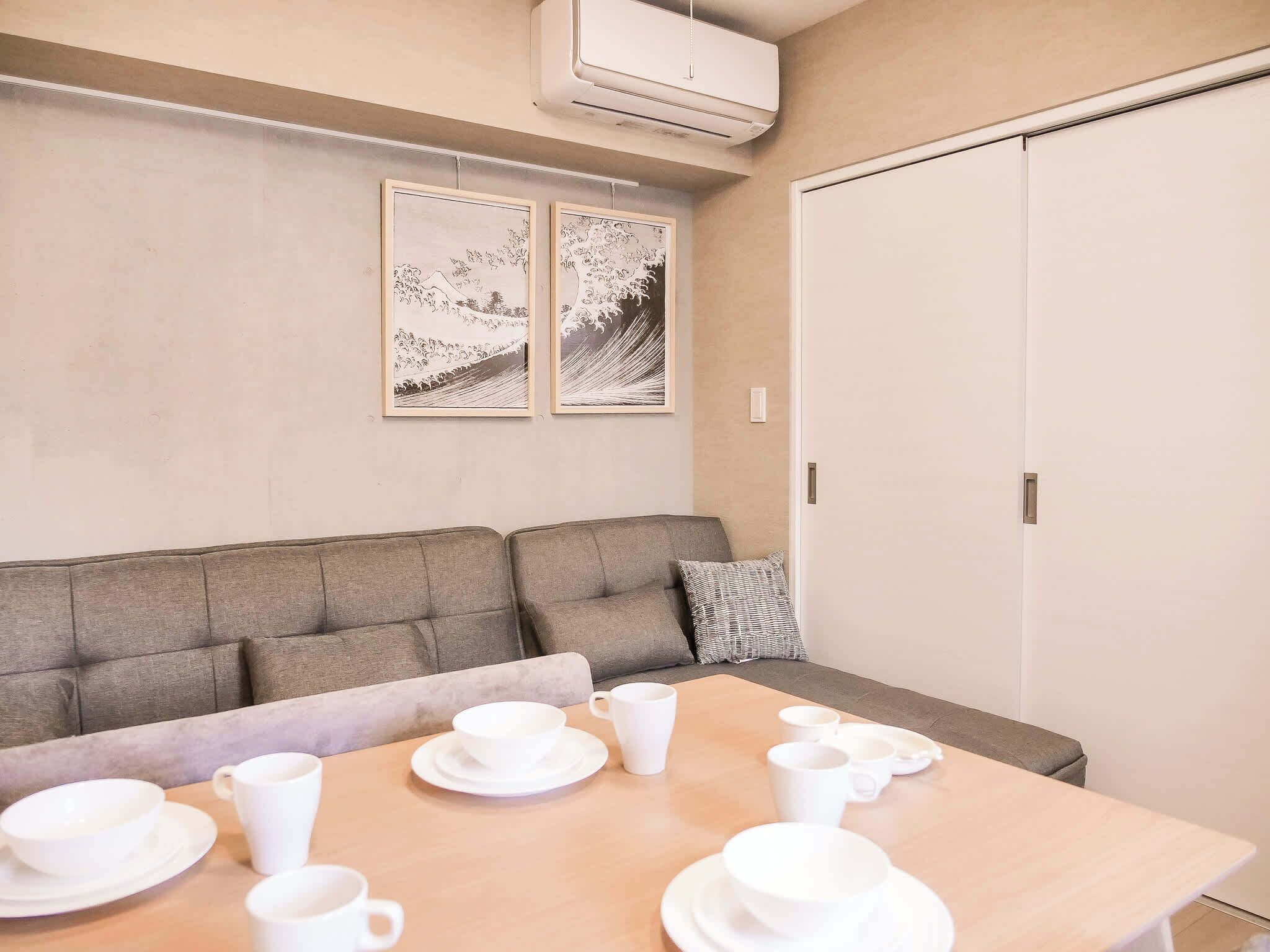 Ein Zimmer mit einer Couch, einem Tisch mit weißen Tassen und Untertellern sowie zwei gerahmten Bildern an der Wand.