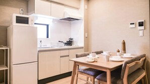 A compact kitchen with white cabinets, a microwave, and a stove. There is a dining table with chairs and a small trash bin. - Triphome Asakusa Alpha 2 Bedrooms (Taito City)