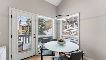A modern dining area with a round table, chairs, and a view of a snowy landscape through large windows.