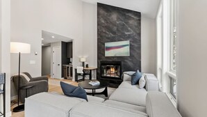 Ein modernes Wohnzimmer mit Kamin, grauen Sofas und einem Essbereich.