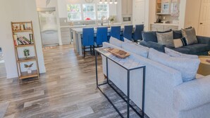 Una cocina moderna con una isla central, sillas azules y un sofá gris en la sala.