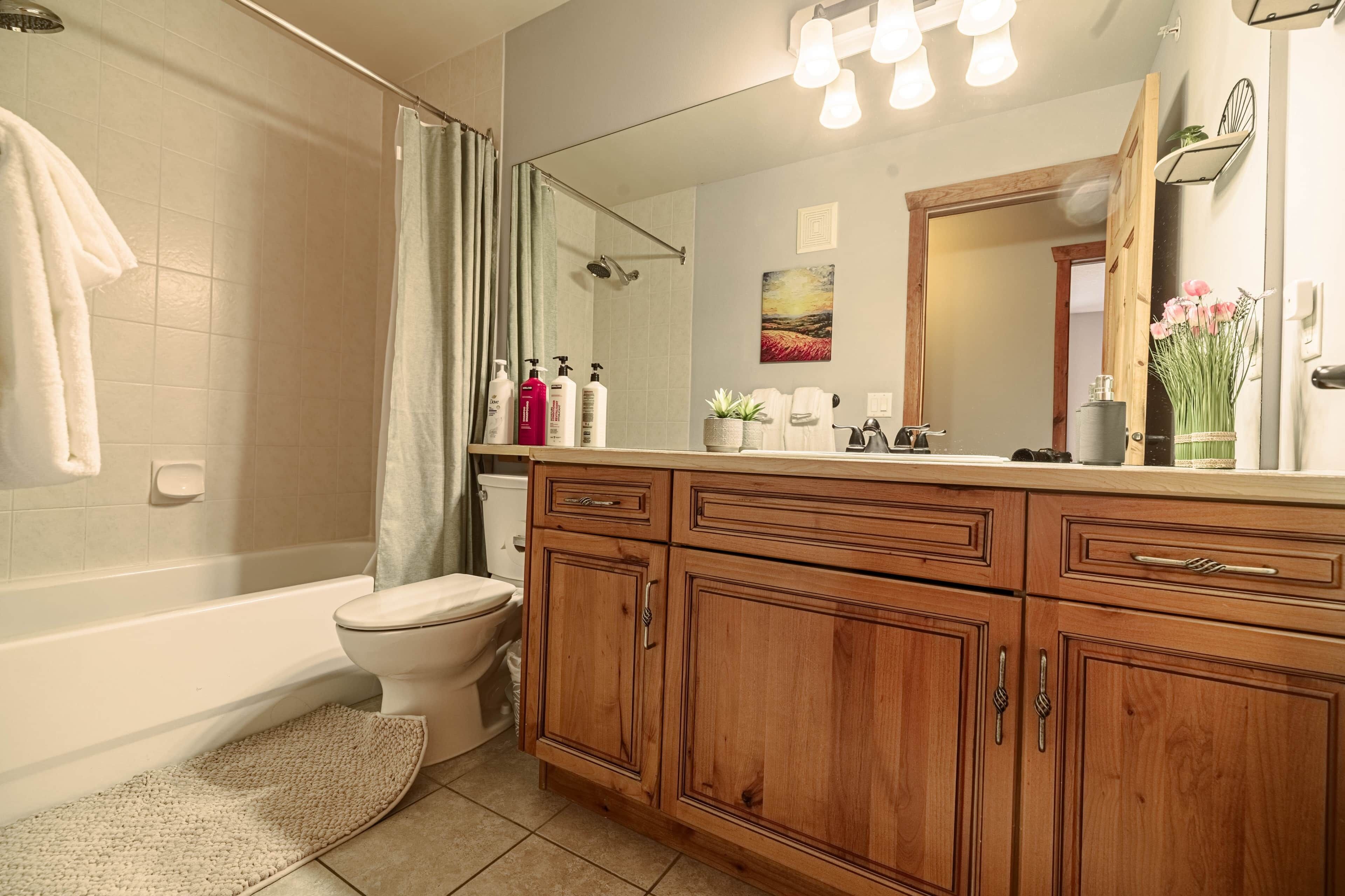 Une salle de bain avec une baignoire, des toilettes, un meuble-lavabo en bois et un grand miroir.