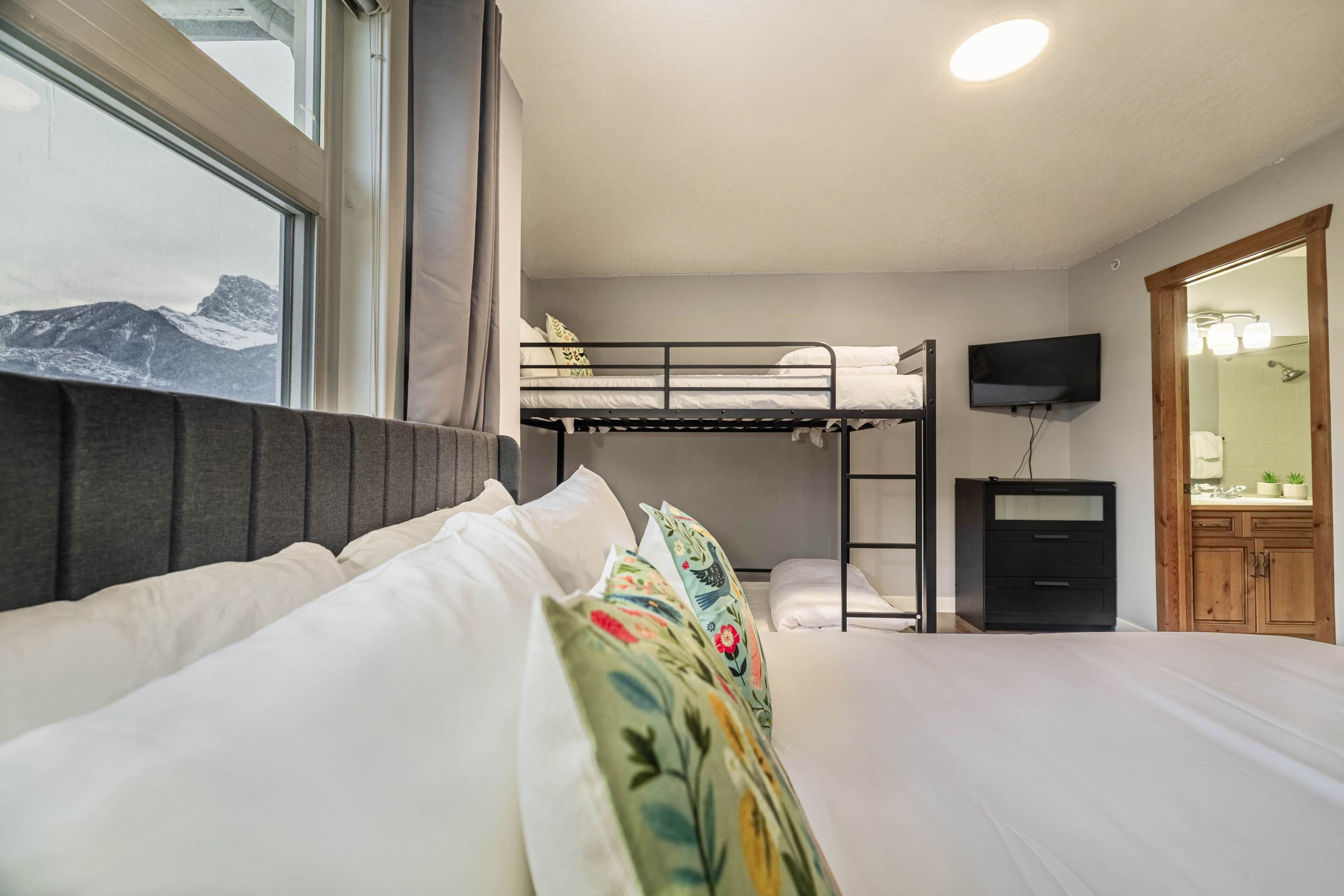 A bedroom with a bunk bed, a bedside table, a TV, and a wooden wardrobe.