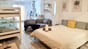 Een moderne hotelkamer met een stapelbed, een slaapbank, een bed en een kitchenette op de achtergrond.