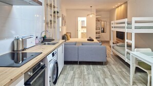 Een compacte hotelkamer met kitchenette, slaapbank, stapelbed en wasmachine.