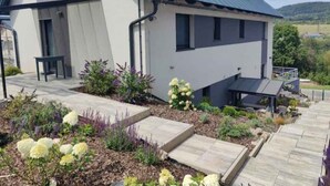 A modern house with a sloped roof, a front porch, and a garden with flowers.