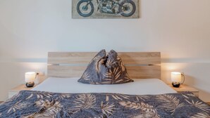A bedroom with a bed, a headboard, a pillow, two bedside lamps, and a wall-mounted motorcycle painting.
