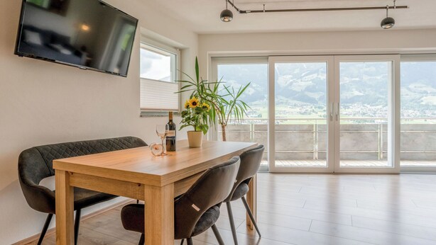 A modern dining area with a wooden table, two chairs, a potted plant, and a bottle of wine.