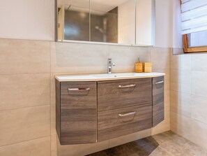 A bathroom with a white sink, dark wood cabinet, and a mirror above the sink. - Apartment Josef by Interhome (Fügen)