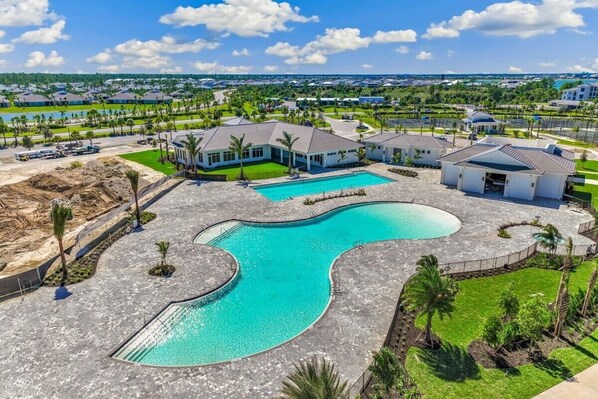 A residential area with a large swimming pool, multiple houses, and a well-maintained lawn.