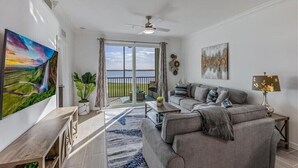 Ein Wohnzimmer mit einer Couch, einem Couchtisch und Kunstwerken. Ein Balkon bietet Blick auf den Ozean.