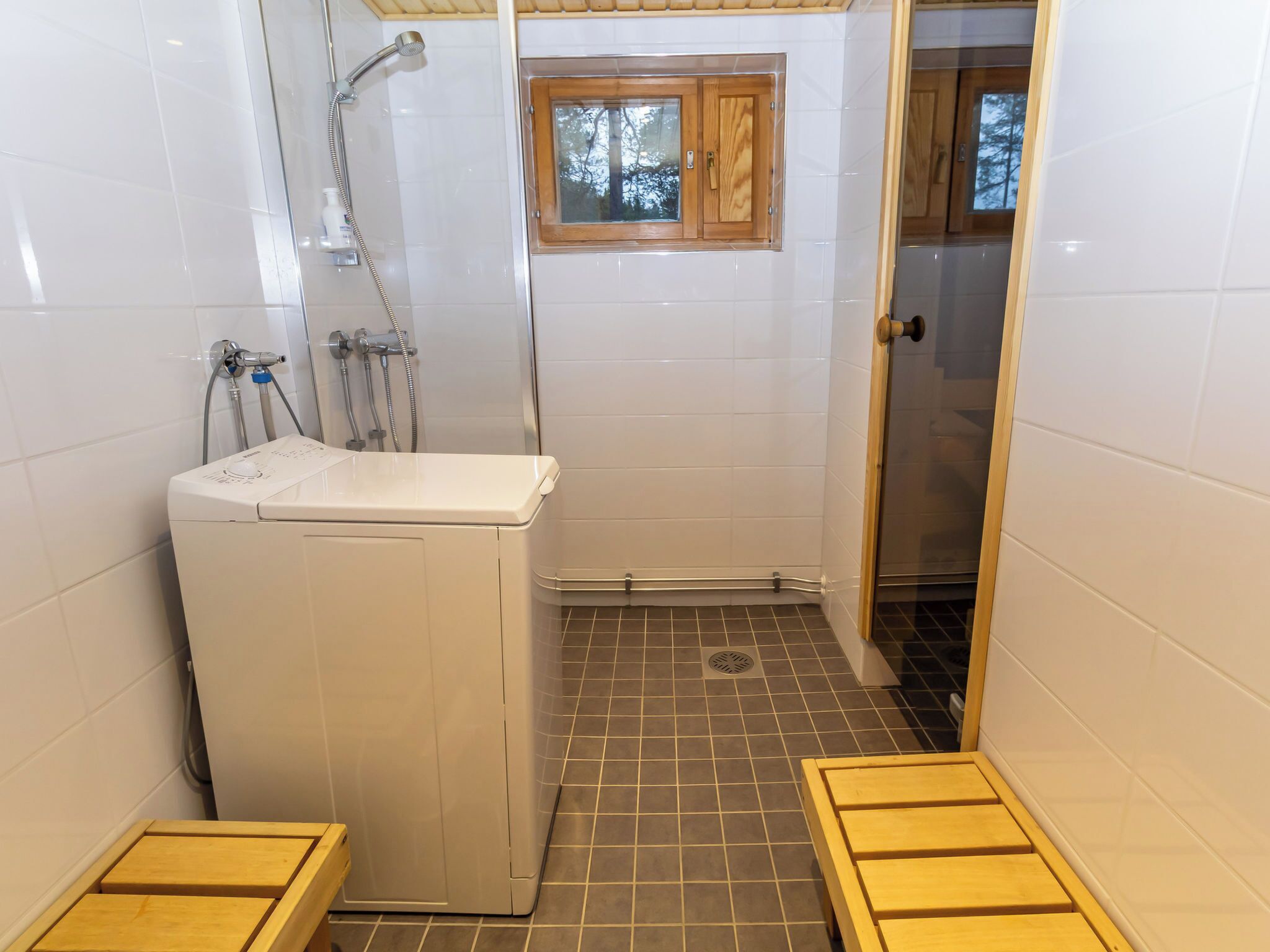 A compact bathroom with a washing machine, a shower, and a small window.