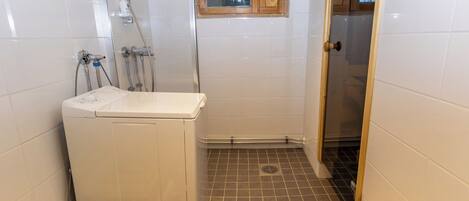 A compact bathroom with a washing machine, a shower, and a small window.