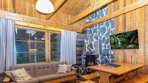 L’intérieur chaleureux d’un chalet avec une cheminée en pierre, des meubles en bois et un téléviseur fixé au mur.