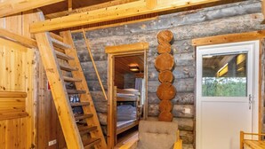 L’intérieur d’une cabane en rondins, avec une échelle en bois, des lits superposés, un fauteuil rembourré et une porte dotée d’une fenêtre.