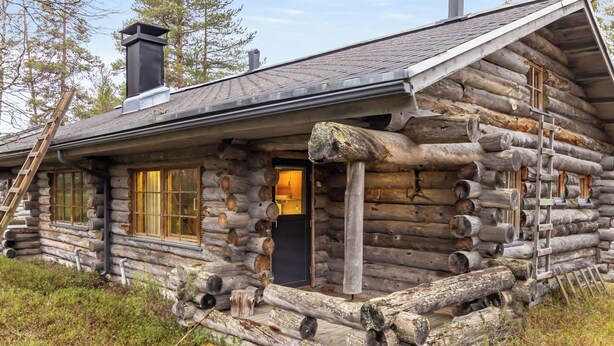 Une cabane en rondins avec une porte d’entrée, des fenêtres et une cheminée.