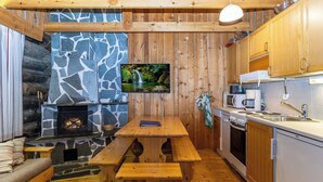 L’intérieur chaleureux d’un chalet avec une cheminée en pierre, une table à manger en bois et un coin cuisine.