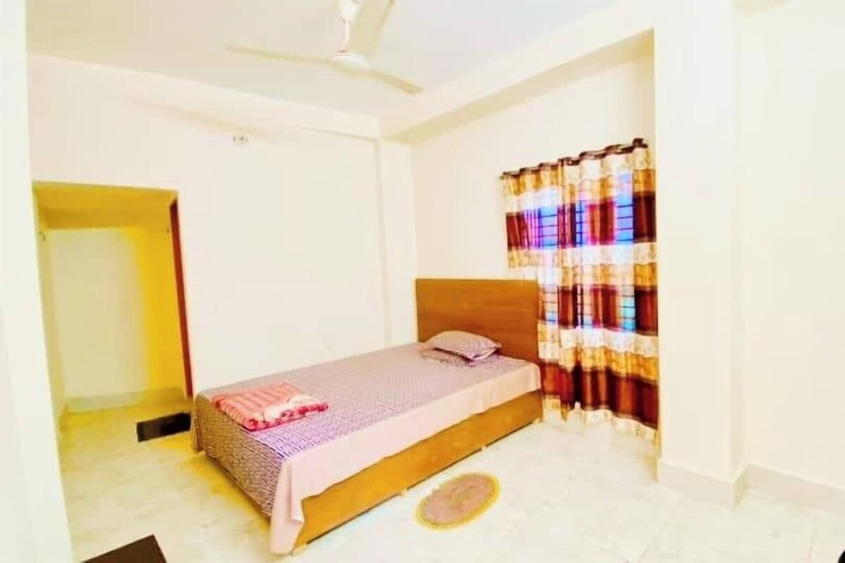 A bedroom with a single bed, a ceiling fan, and a window with colorful curtains.