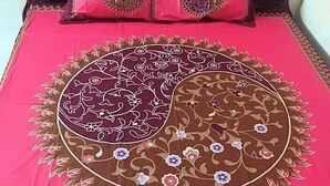 A bed with a red bedspread featuring a large circular design with floral patterns and a fringe border. - Heaven beach Resort Saint Martin (Saint Martin's Island)