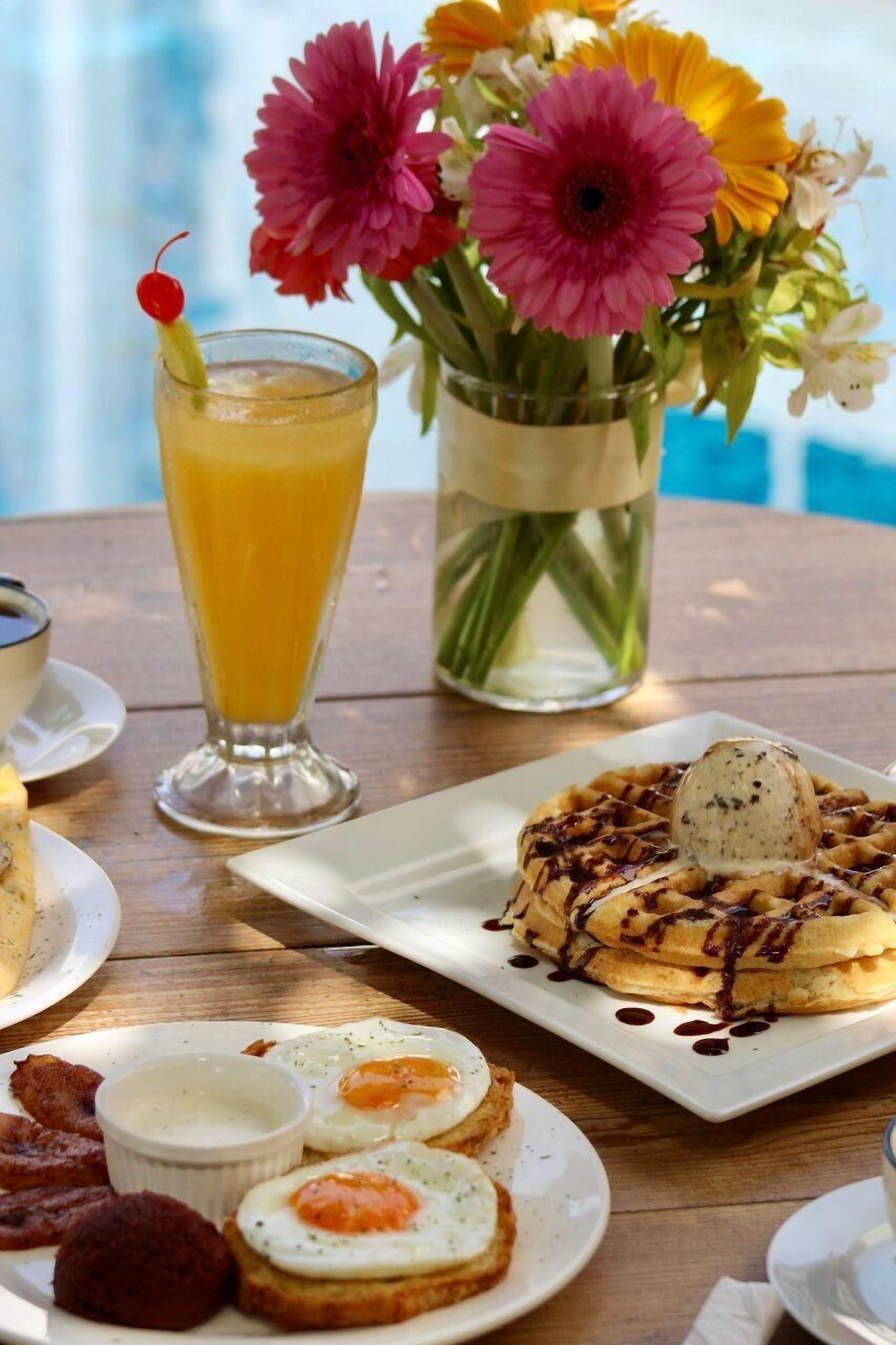 A breakfast setting with waffles, eggs, and a glass of orange juice.