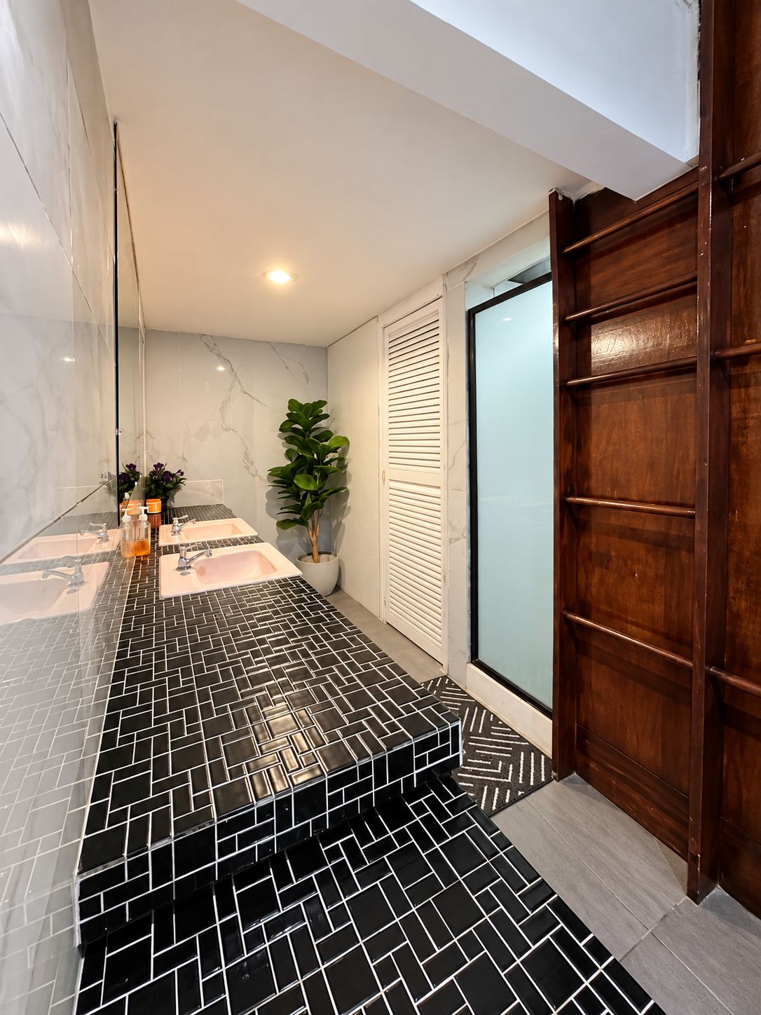 A modern bathroom with a black and white tiled floor, a large mirror, and a wooden door.