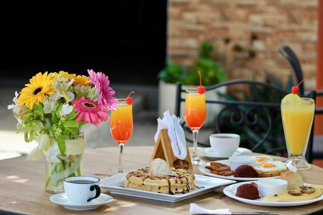 Una mesa de madera con una variedad de alimentos, bebidas y un arreglo floral para el desayuno.