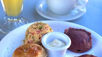 A plate with food items including a muffin, a small bowl of sauce, and roasted plantains, accompanied by a cup of coffee and a glass of orange juice.
