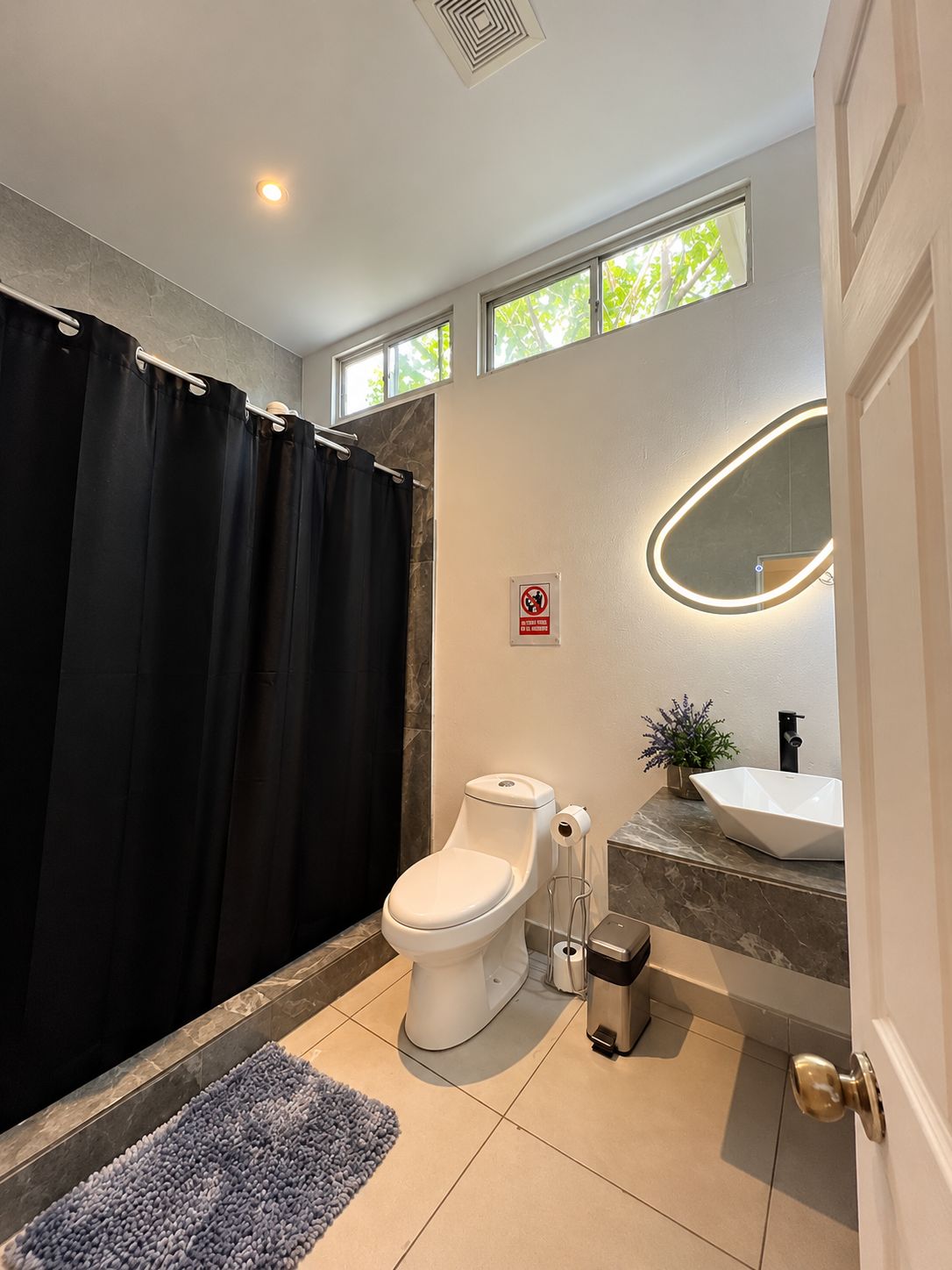 Un baño moderno con inodoro, lavabo, cortina de ducha, espejo y una pequeña planta en maceta.