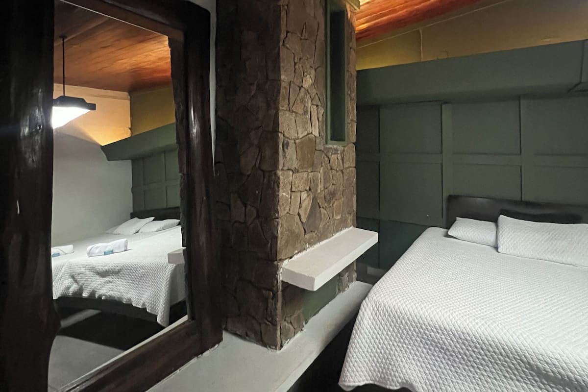 A room with two beds, a stone accent wall, and a wooden ceiling.