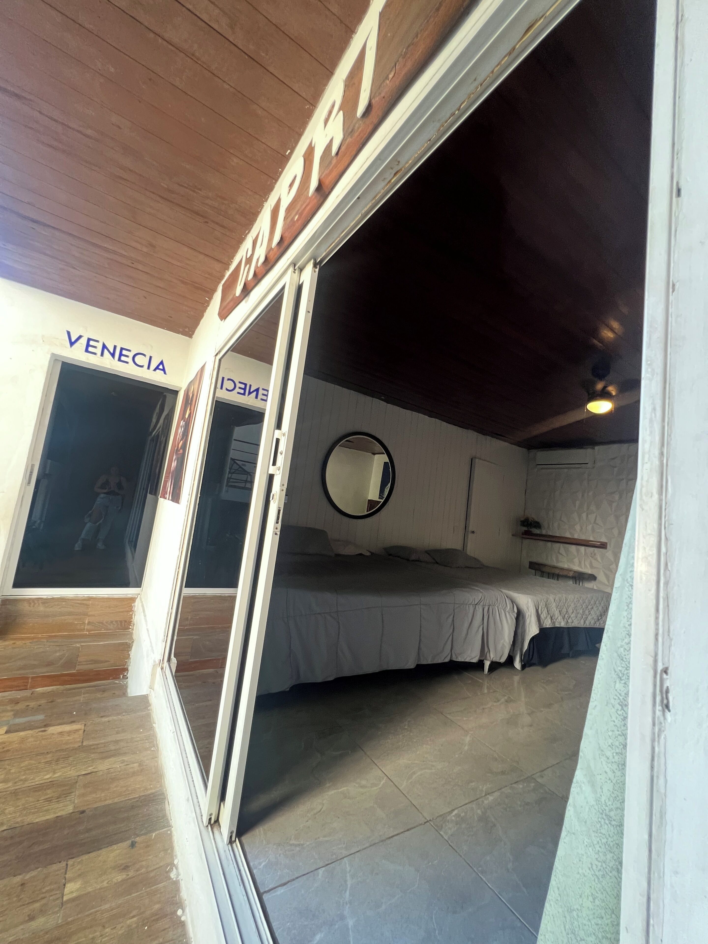 A room with a bed, a mirror, and a wooden ceiling. There is a door labeled "VENEZIA" and a sign with "ENERGY" on it.