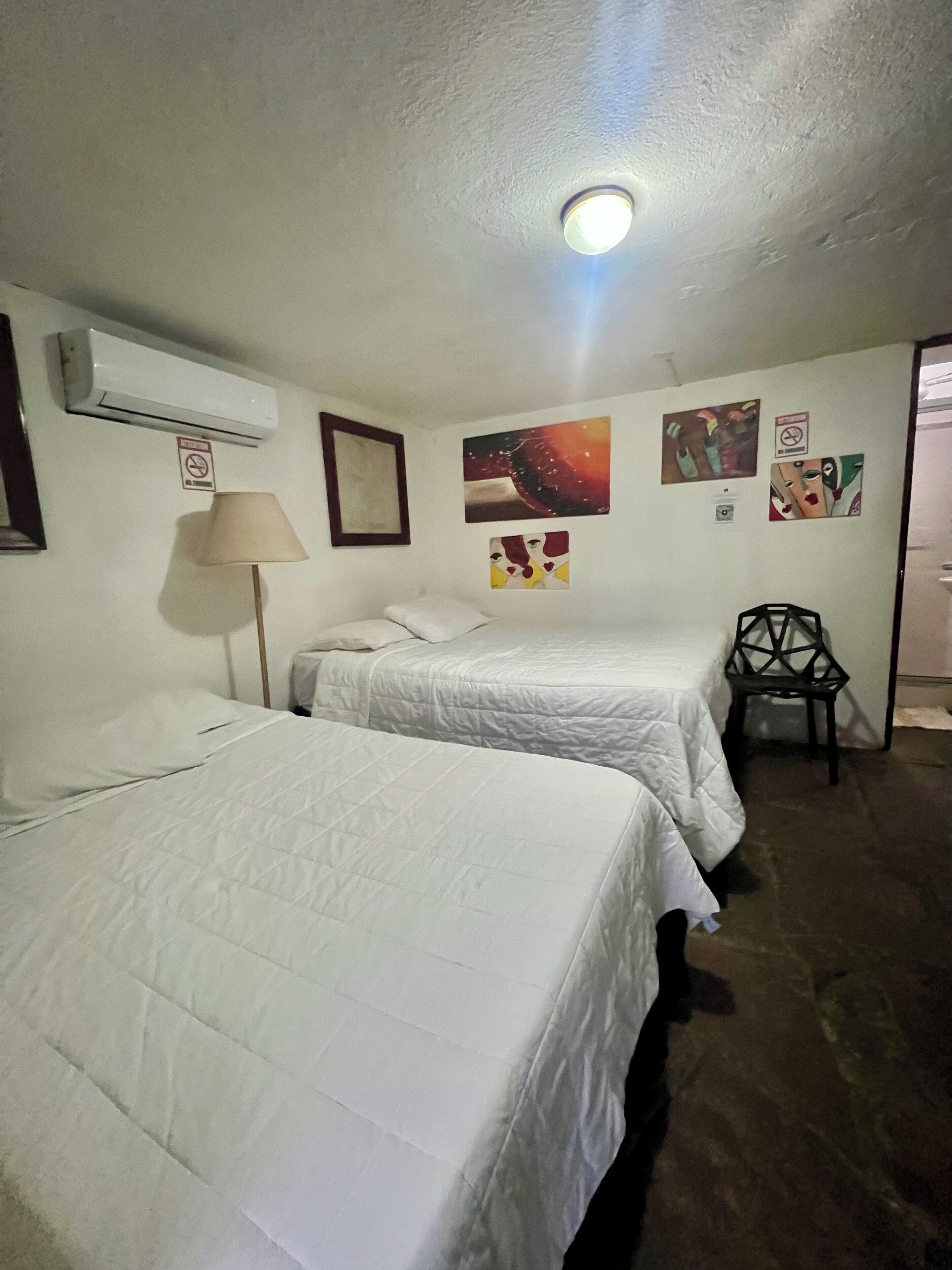 A hotel room with two beds, a chair, and artwork on the walls.