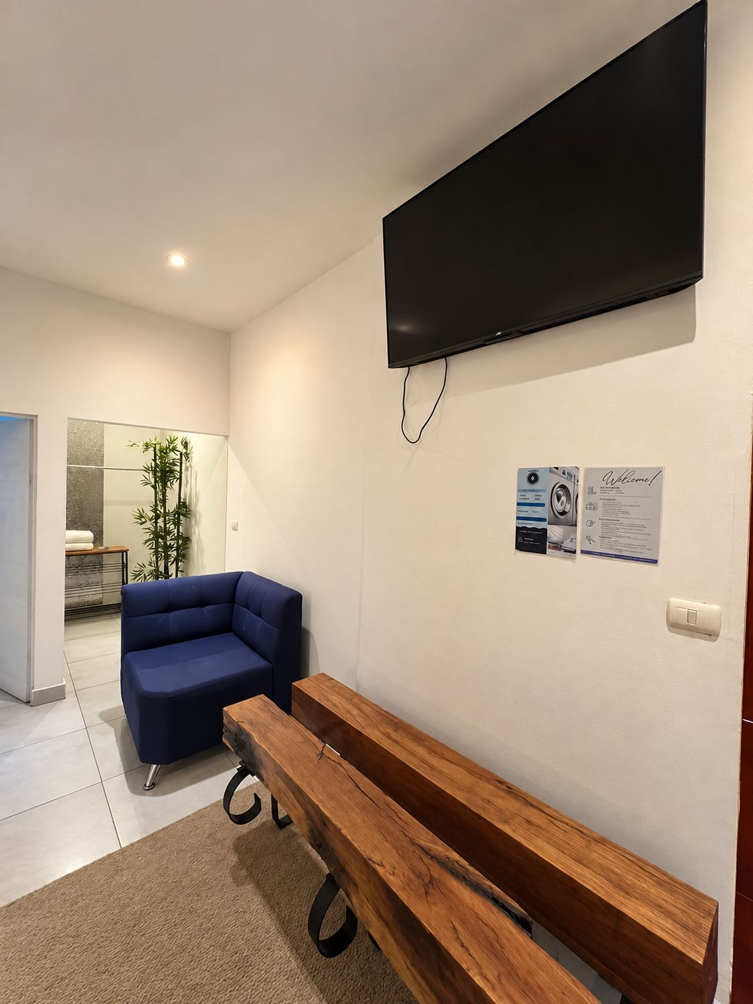 Een moderne kamer met een flatscreen televisie aan de muur, een blauwe bank, een houten bankje en een kleine tafel.