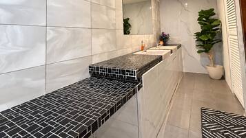 A modern bathroom with a marble wall, a black and white tiled countertop, a mirror, and a potted plant.