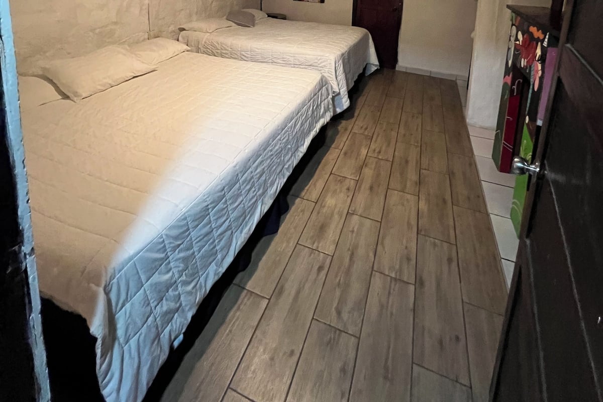 A narrow room with two beds, wooden flooring, a door, and a wall with a 'No Smoking' sign.