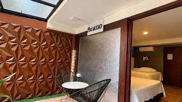 A hotel room with a bed, a small table, and a chair. There is a sign that says 'Picasso' on the wall.