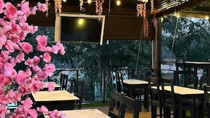 An outdoor seating area with tables and chairs, hanging floral decorations, and string lights. - Hotel Villa Napoli (Santa Ana)