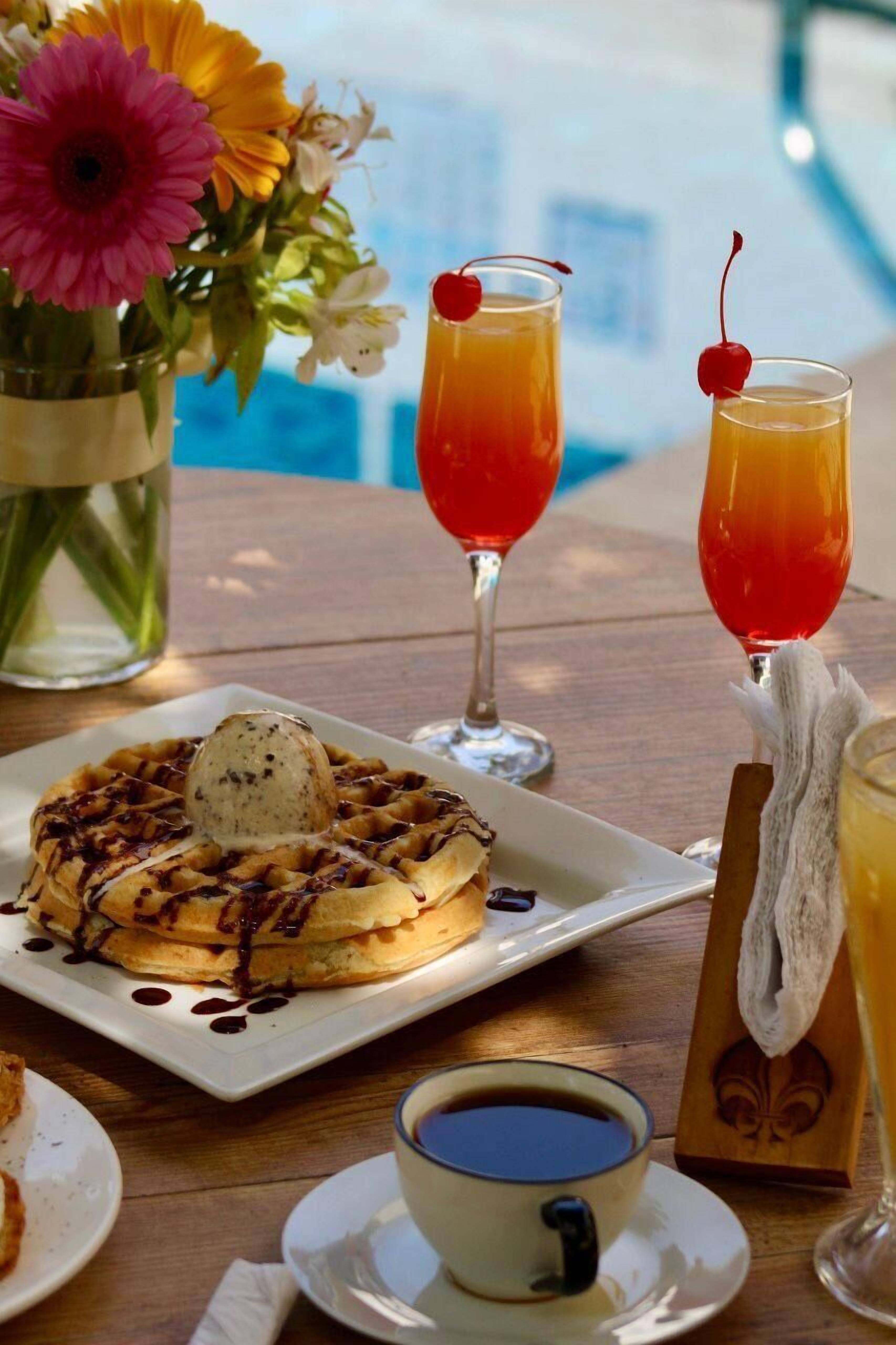 A breakfast setting with waffles, a cup of coffee, and two glasses of orange juice with cherries.