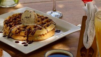 A breakfast setting with waffles, a cup of coffee, and two glasses of orange juice with cherries.