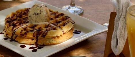 A breakfast setting with waffles, a cup of coffee, and two glasses of orange juice with cherries.