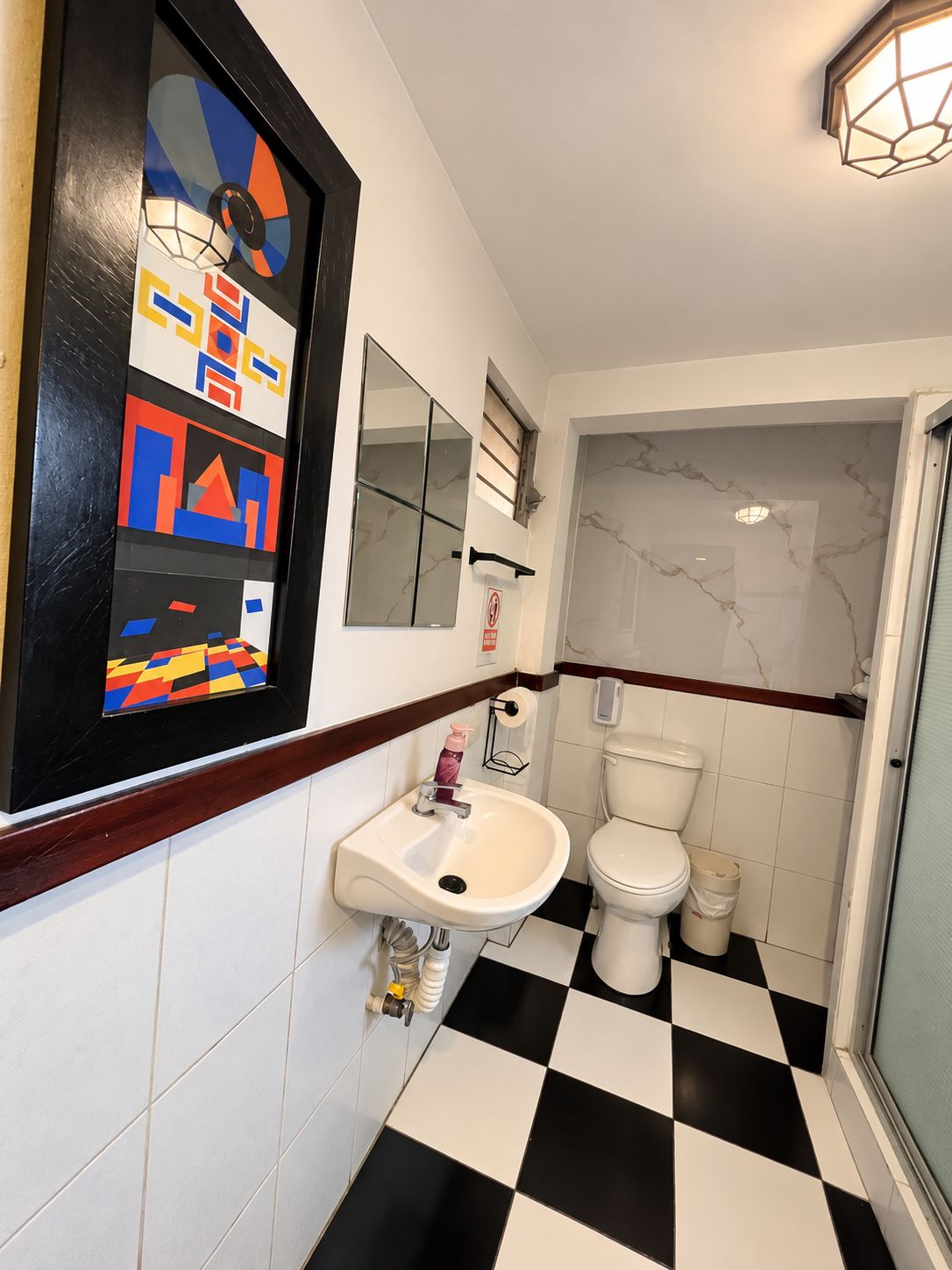 Un baño con piso a cuadros blanco y negro, un lavamanos blanco, un inodoro y un espejo sobre el lavamanos.