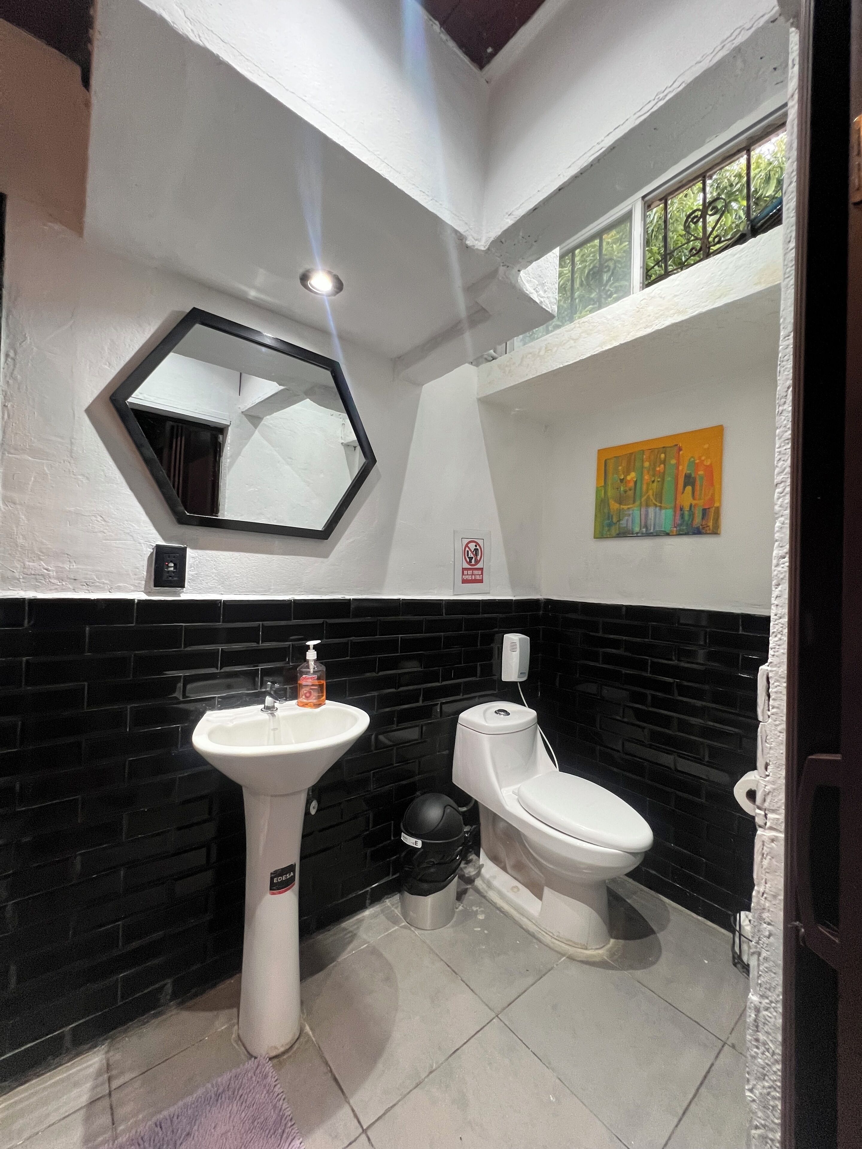 A bathroom with a white sink, a toilet, a black tiled wall, a mirror, and a small window.