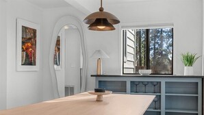 Une cuisine moderne avec une table en bois, un luminaire suspendu et une fenêtre donnant sur la forêt.