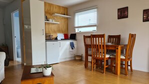 Eine kleine Küche mit Kühlschrank, einem Holzschrank und einem Essbereich mit Tisch und Stühlen.