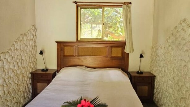 A bedroom with a wooden ceiling, a large bed, a window with curtains, and stone walls.
