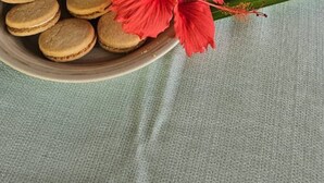 A plate of cookies and a red flower on a table with four glasses of yellow liquid.