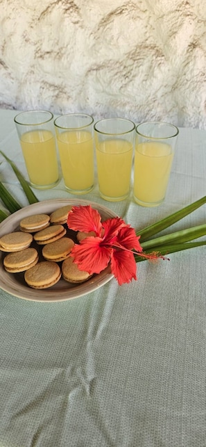A plate of cookies and a red flower on a table with four glasses of yellow liquid.