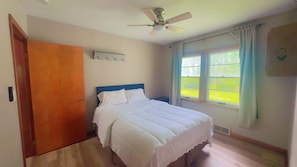 A bedroom with a bed, a ceiling fan, a window with curtains, and a door.