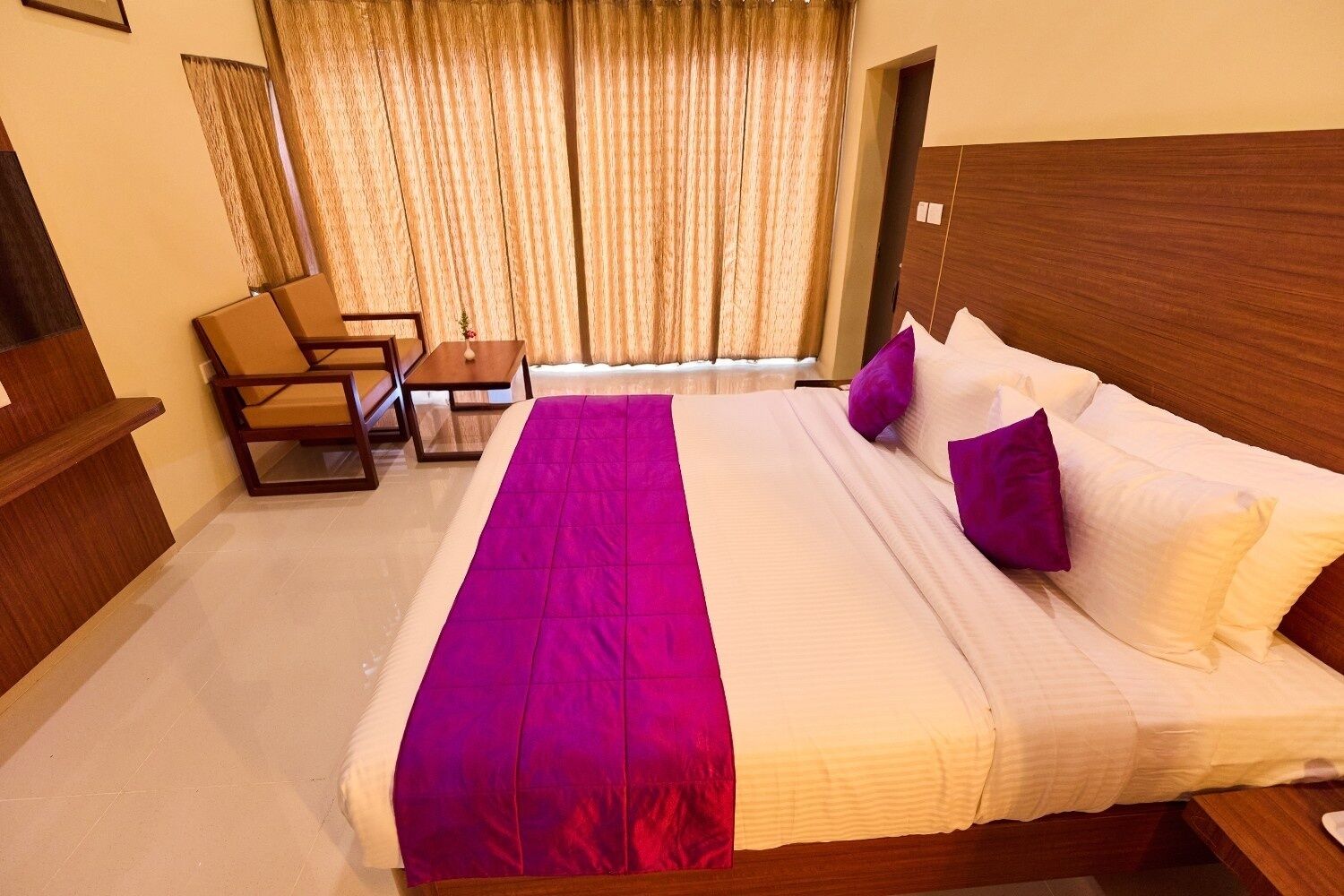 A hotel room with a large bed, a wooden headboard, a small table, and a chair.