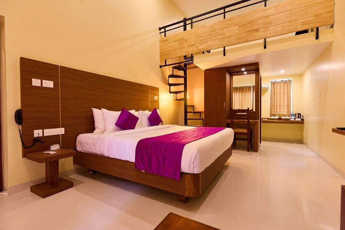 Une chambre d’hôtel moderne avec un lit en bois, un bureau et un petit coin salon.